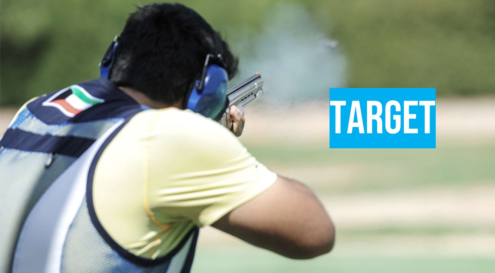 A person wearing ear protection and a shooting vest aims a shotgun outdoors, with the word "TARGET" displayed to the right.