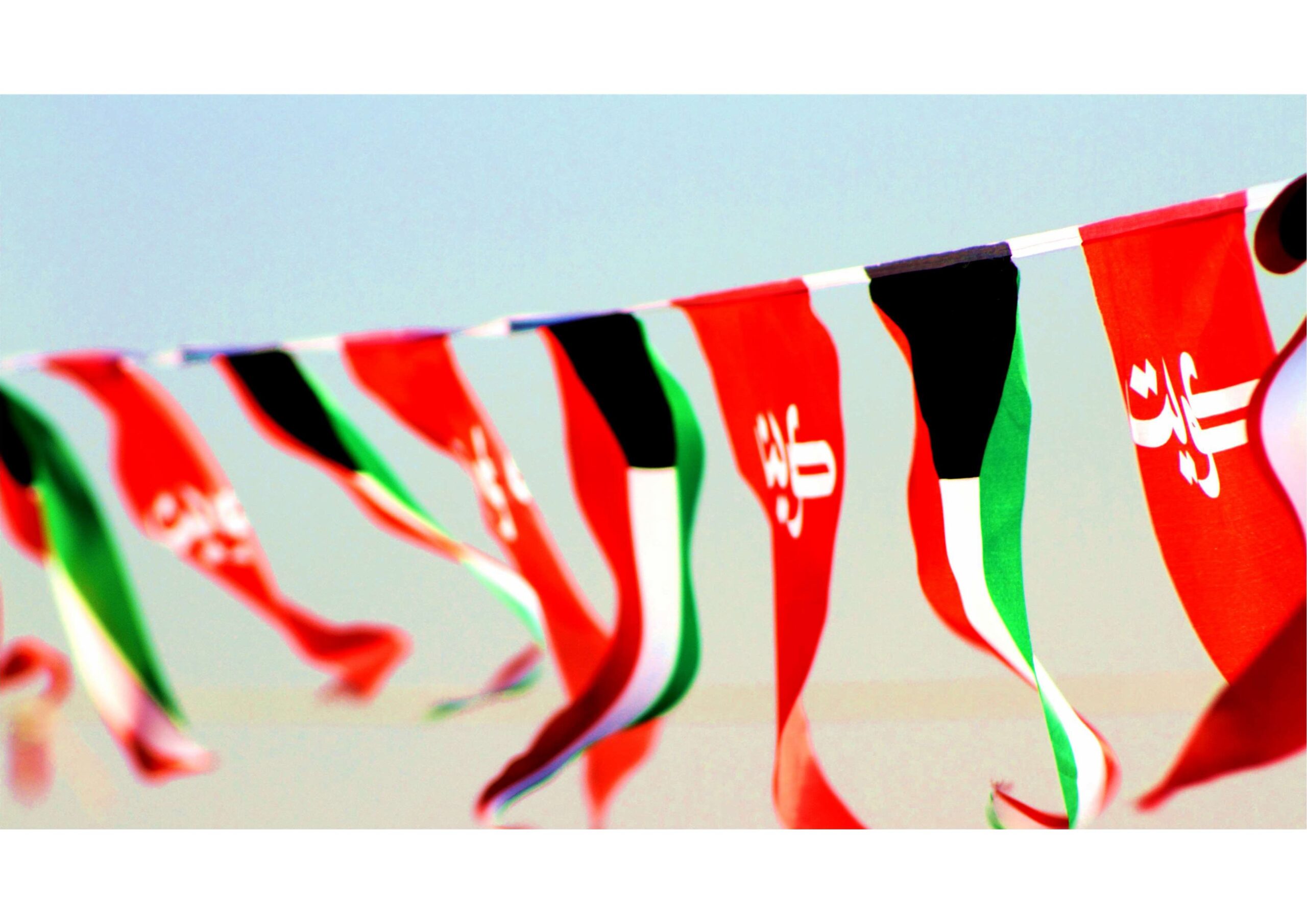 A row of Kuwait national flags and flag bunting waving in the wind against a clear sky.
