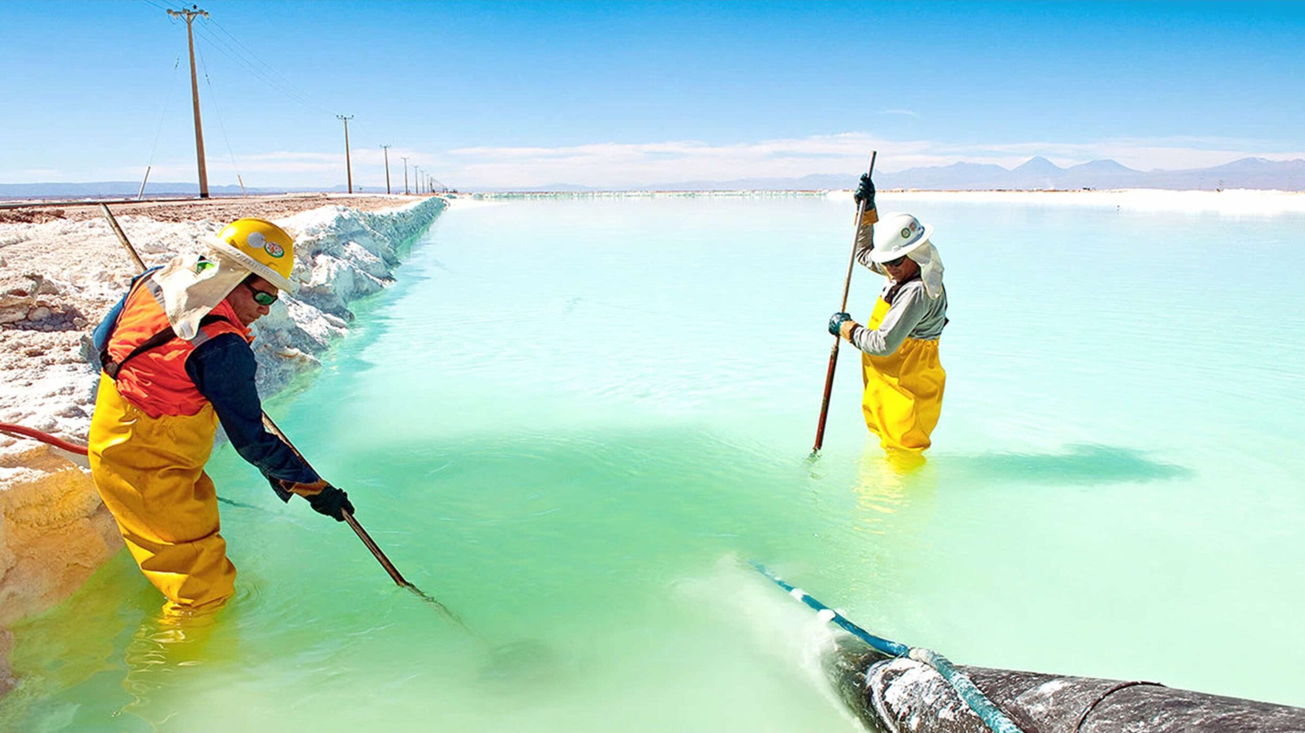 A firefighter stands in front of a damaged car with a pile of bricks fallen onto its hood; rubble and debris are visible in the background.