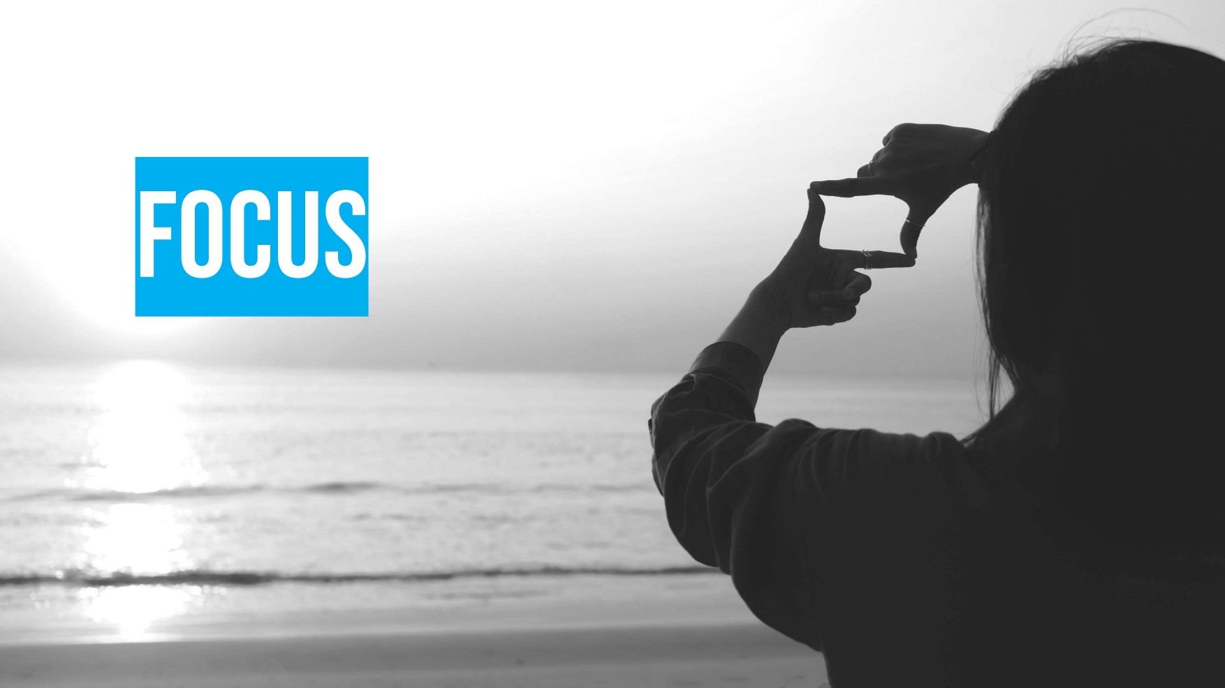 A person at the beach frames the sunset with their hands; the word "FOCUS" appears in bold white text on a blue background.