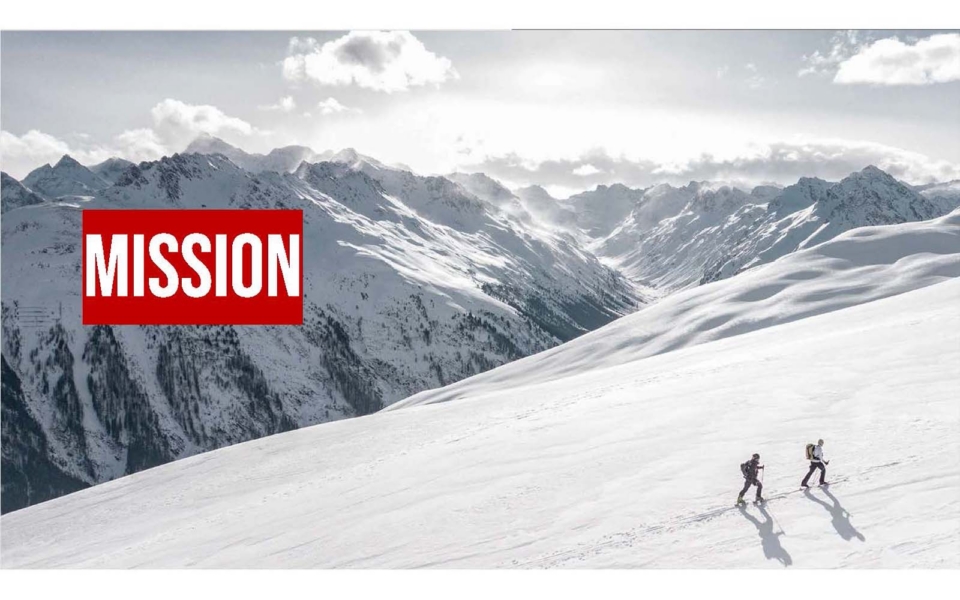 Two people hike up a snowy mountain slope with snow-covered peaks in the background; the word "MISSION" in bold red text appears on the left.