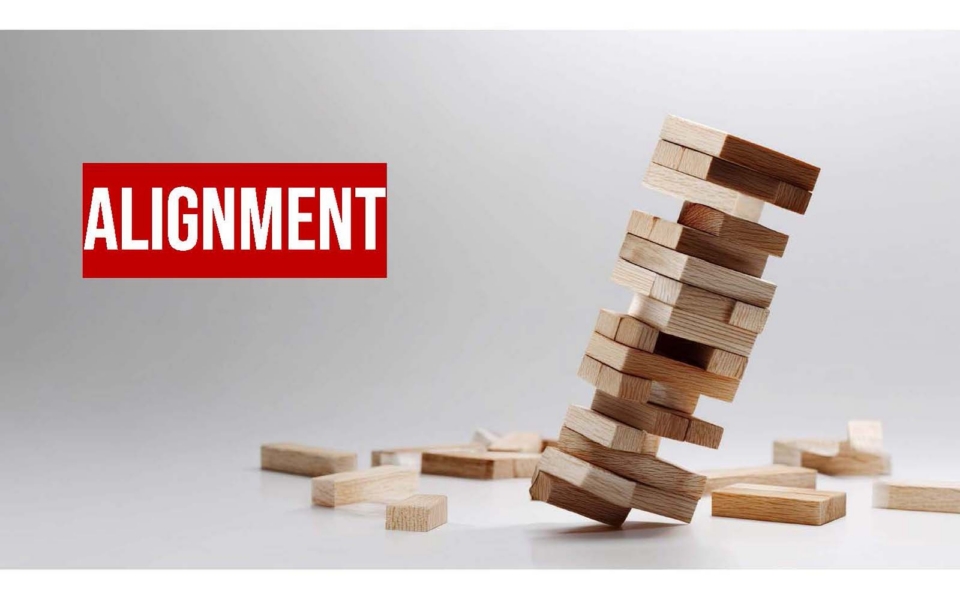 A leaning stack of wooden blocks is about to fall, with the word "ALIGNMENT" in bold white letters on a red background to the left.